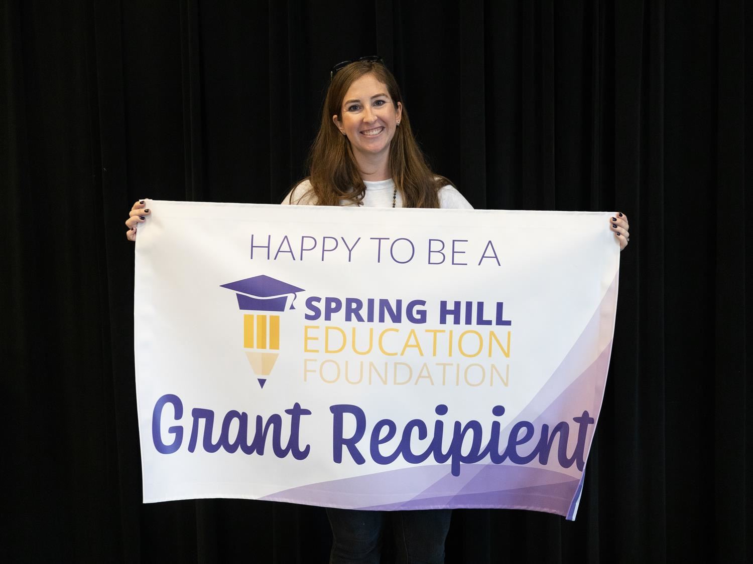 Anna Manning smiling with the "Happy to be a SHEF Grant Recipient" banner